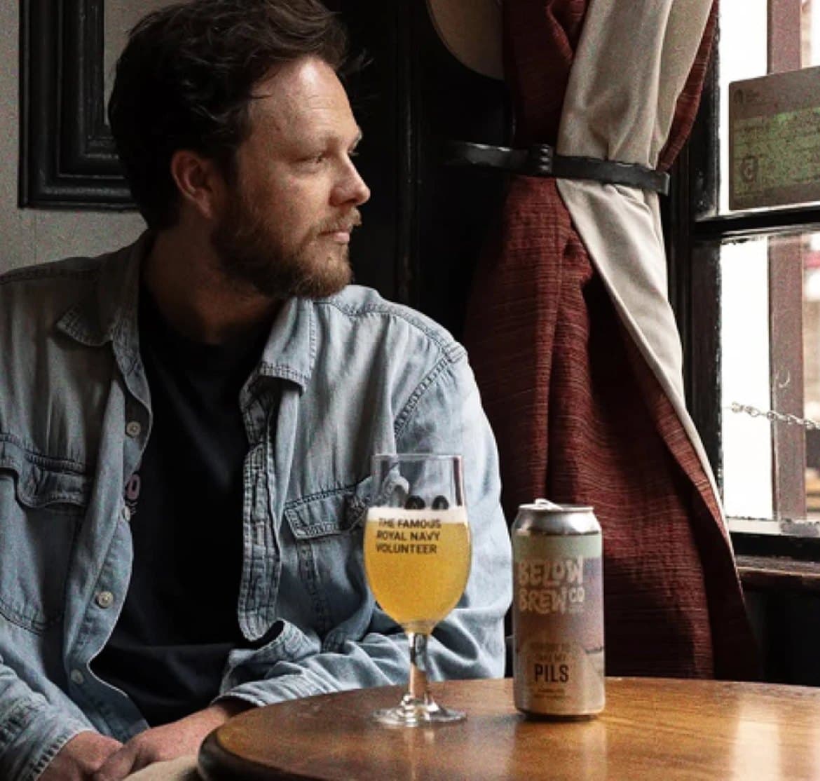 Rob, co-founder of Below Brew Co, at a pub table by the window with a glass and a can of Below Brew Pils